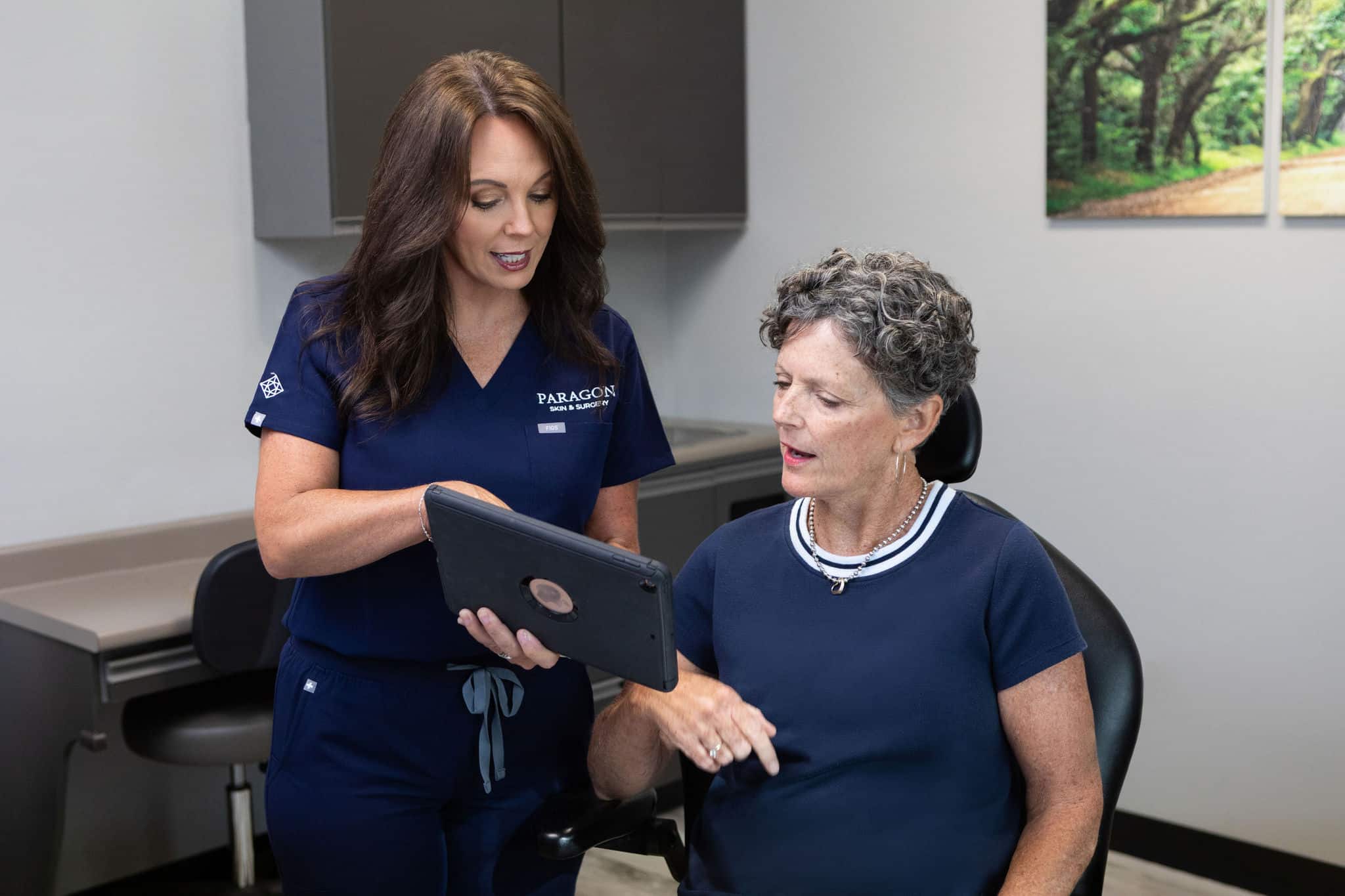 f-8625 Dermatologist consulting a patient with a tablet in a clinic setting.