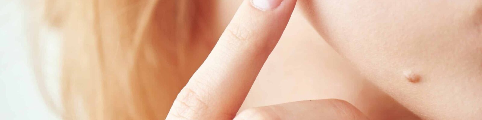 Close-up of a finger pointing at a mole on skin, related to skin health.